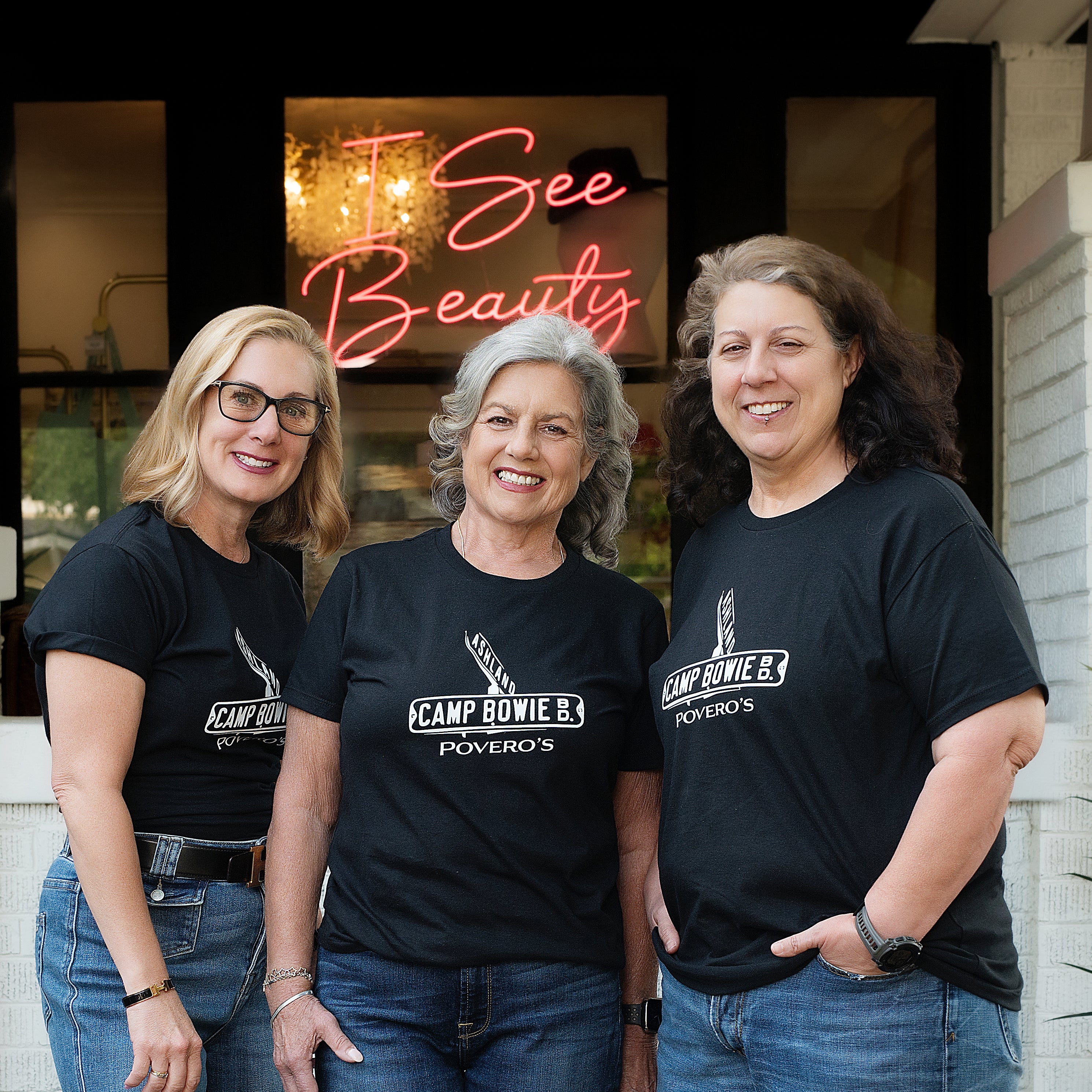 Jenilee, Darlene, and Bobbi standing together outside of Povero's with the I see beauty neon sign in the background.