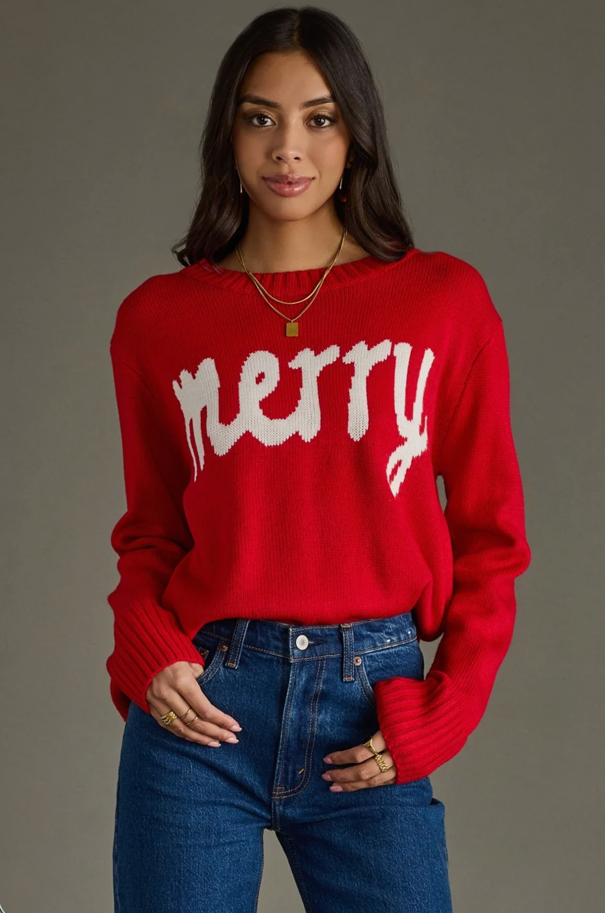 Model wearing a red knit sweater with white Merry text, front view