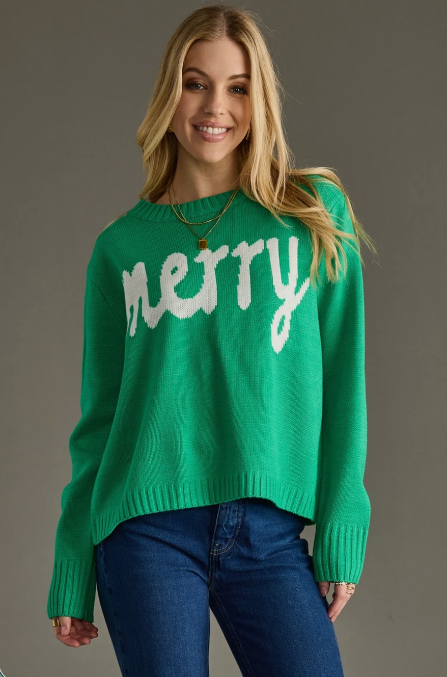 Model wearing a kelly green knit sweater with white Merry text, front view