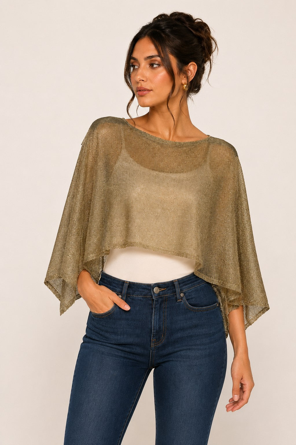 Model wearing a gold lurex knit crop poncho with sheer draped sleeves over jeans